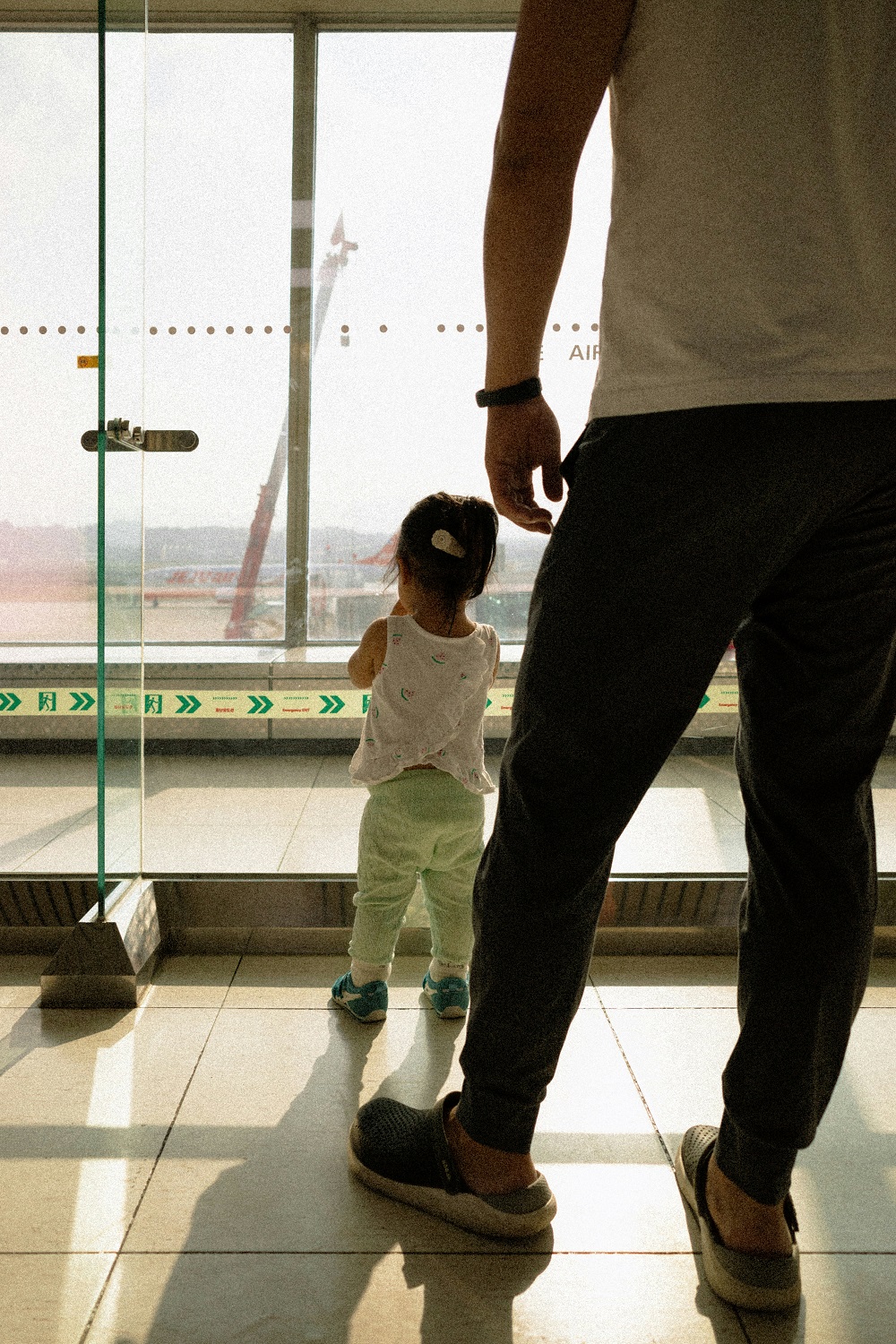 A parent and small child watching planes through an airport window