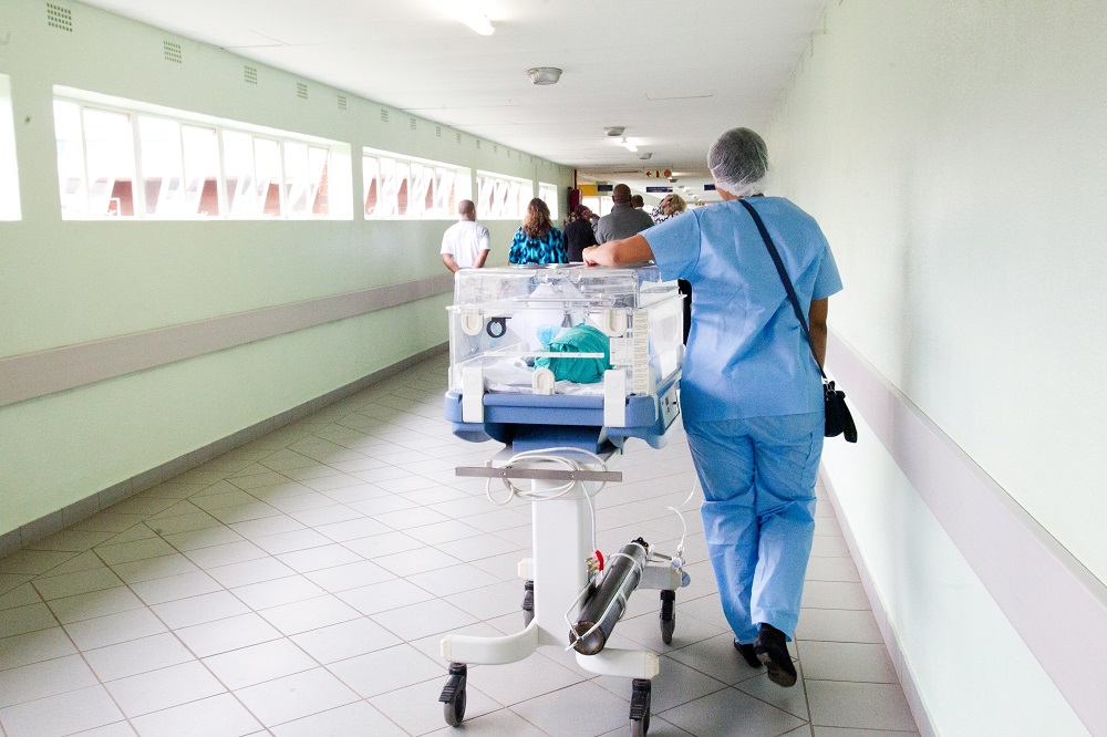A nurse moving an incubator along a hospital corridor