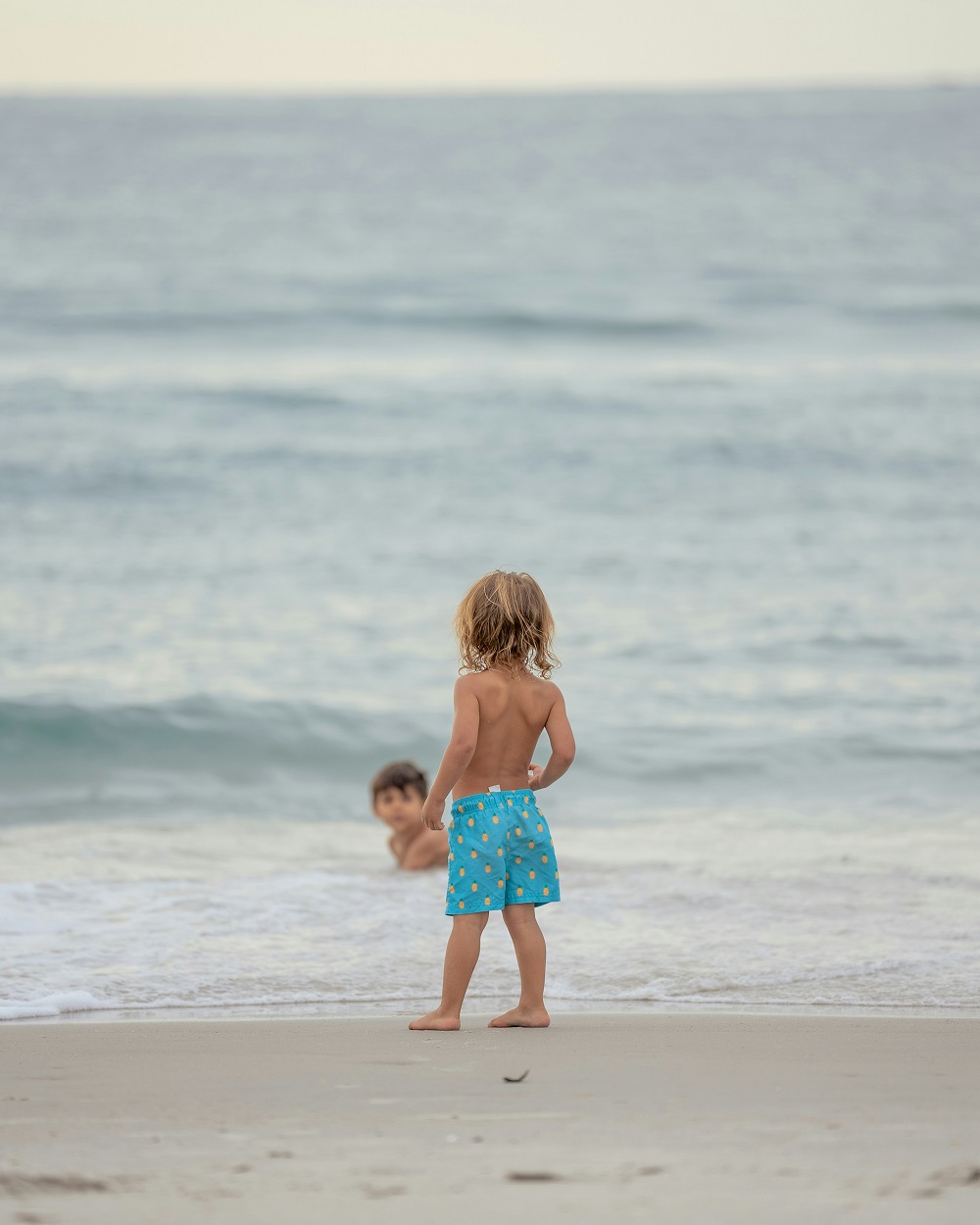 Two young children playing at the water’s edge on a beach